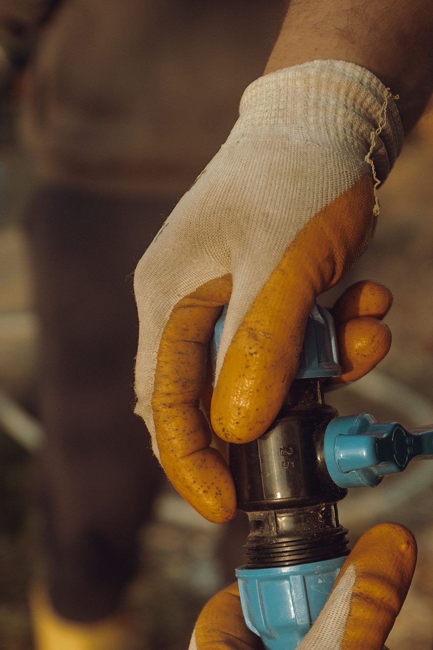 Licensed stock photograph: two gloved hands tightening a compression fitting on a water line.