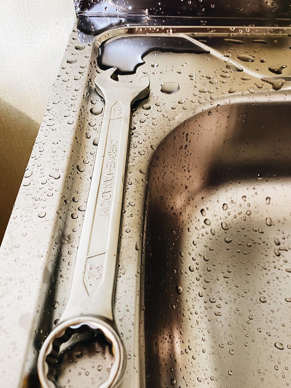 Licensed stock photograph: a combination wrench lying on the wet stainless steel rim of a kitchen sink.